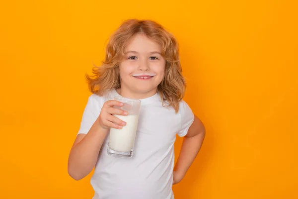 Kid drink milk with funny emotions on yellow background. Child drinking milk, studio portrait. Cute child with milk moustache hold a glass of milk
