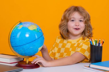 Little student school child looking at globe during geography lesson isolated on studio background. Portrait of nerd student with school supplies