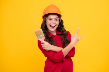Miğferli çocuk müteahhidi. Fırça aletli ya da boya silindirli genç kız ressam. Sarı arka planda izole edilmiş tamir işindeki çocuk. Çocuk yenileme konsepti. Mutlu genç kız