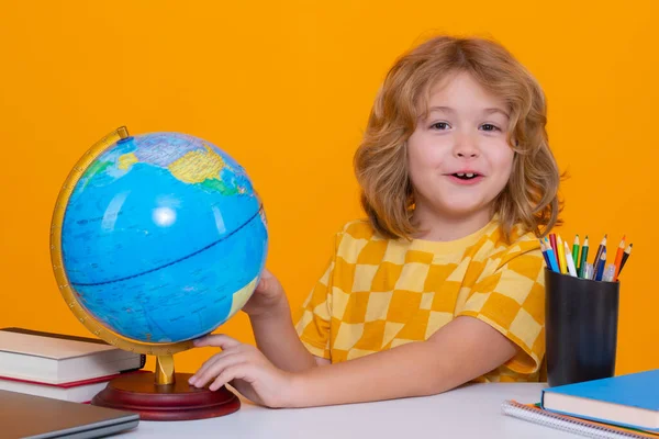 Little student school child looking at globe during geography lesson isolated on studio background. Portrait of nerd student with school supplies