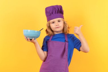 Kid chef cook with cooking bowl. Kid in cooker uniform and chef hat preparing food on studio color background. Cooking, culinary and kids food concept