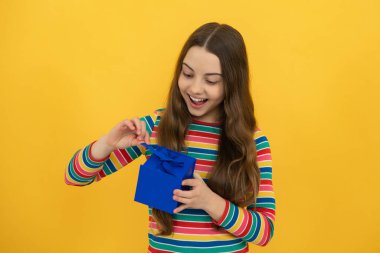 Sarı izole edilmiş arka planda hediye kutusu tutan ergen bir çocuk. Çocukların doğum günü hediyesi. Noel veya Yeni Yıl hediye kutusu