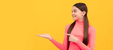 happy child pointing finger on copy space on yellow background, offer. Child face, horizontal poster, teenager girl isolated portrait, banner with copy space