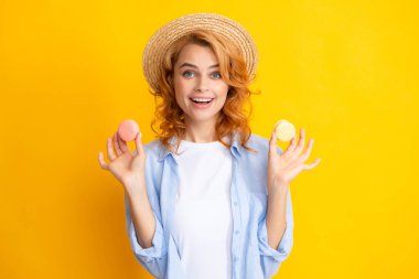 Tatlı, genç bir kadın. Kurabiye tutuyor. Güzel gülümseyen genç kız sarı arka planda renkli badem kurabiyeleri yiyor.