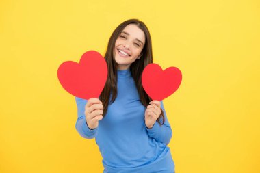 Sevgililer Günü. Ellerinde kalbi olan güzel genç bir kadın. Sarı arka planda kağıt kalpli çekici bir kadın.