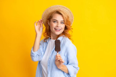 Portakal sarısı arka planda dondurma yiyen güzel bir kadının portresi. Çikolatalı dondurma yiyen yaz şapkalı bir kız. Mutlu heyecanlı yüz ifadesi kadın portresi