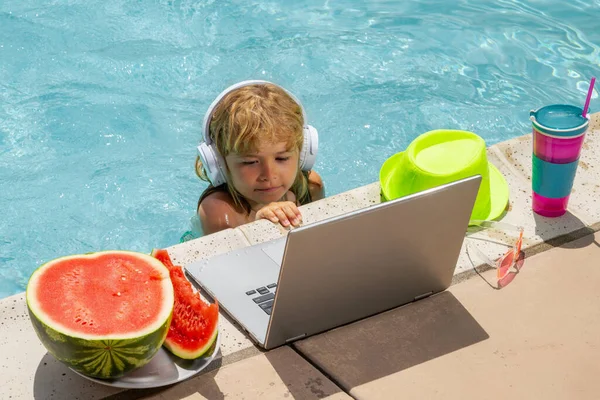 Child work outside with laptop in pool. Kid working on laptop from the swimming pool. Summer business