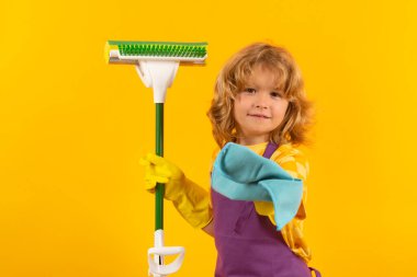 Child doing housework. Children helping with housekeeping, cleaning the house. Housekeeping at home. Cute child boy helping with housekeeping on yellow studio backdround