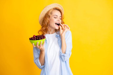 Womans enjoying a fresh sweet cherry. Picking eating cherry fruit. Female eating cherries on yellow background