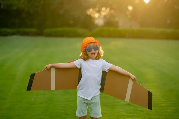Kid pilot with paper wings or toy airplane having fun on meadow. Portrait of child with toy paper wings outdoor. Success, creative and start up concept