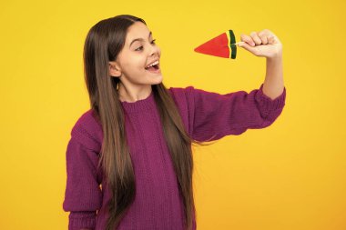 Funny child with lollipop over yellow isolated background. Sweet childhood life. Teen girl with yummy caramel lollipop, candy shop. Teenager with sweet sucker