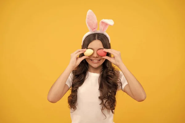 stock image cheerful teen girl in bunny ears hold eggs on yellow background, easter.