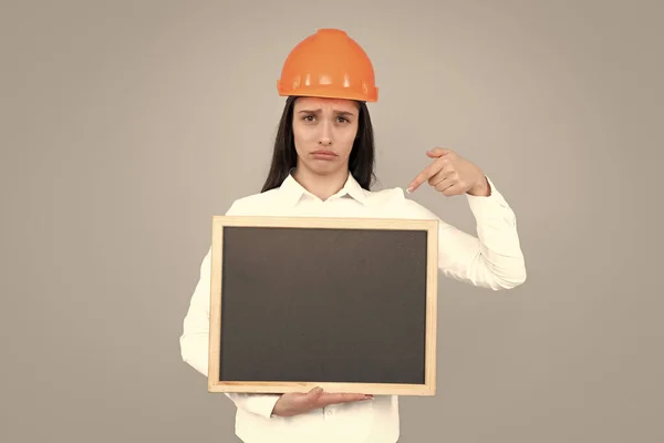 Architect woman in helmet pointing on board over gray background, pointing finger