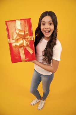 Amazed teenager. Child with gift present box on isolated studio background. Gifting for kids birthday. Excited teen girl