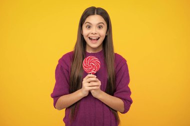 Funny child with lollipop over yellow isolated background. Sweet childhood life. Teen girl with yummy caramel lollipop, candy shop. Teenager with sweet sucker