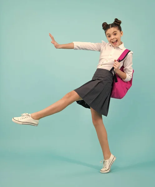 Amazed teenager. Schoolgirl in school uniform with school bag. Teenage girl student on blue isolated background. Jump and run. Learning knowledge and children education concept. Excited teen girl