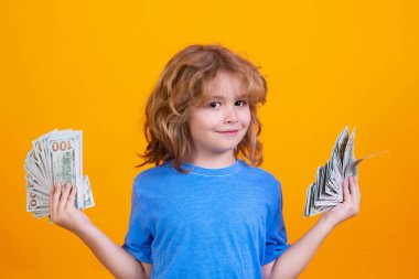 Child with lots of money dollar banknotes isolated over yellow studio background