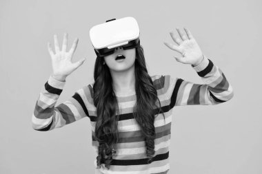 Amazed teenager using VR headset. Kid play vr video game. Digital future and innovation. Child in virtual goggles. Excited teen girl with virtual reality goggles headset isolated on yellow