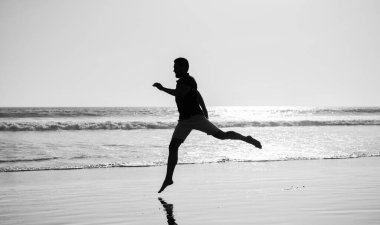 Enerjik bir yaz. Koşucu özgürlüğü hisseder. Acele et. Dayanıklılık ve dayanıklılık. Kısa mesafe silueti. Spor atleti okyanusta kazanmak için hızlı koşar. Sabah sporu aktivitesi. Kumsalda koşan enerjik bir adam..