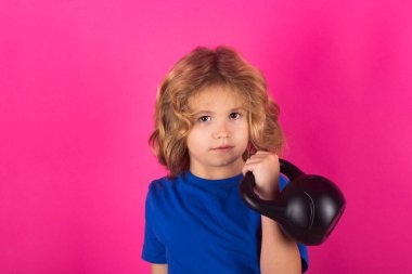 Kid with kettlebell in studio on red pink background. Child boy pumping up biceps muscles with kettlebell. Fitness kids with dumbbells