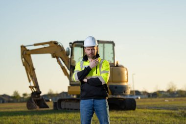 Worker with bulldozer on site construction. Man excavator worker. Construction driver worker with excavator on the background. Construction worker with tractor or construction vehicle at building