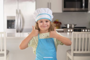 Portrait of funny child chef in kitchen. Chef kid cook baking at home kitchen. Kid chef cook cookery at kitchen. Cooking, culinary and kids. Little boy in chefs hat and apron
