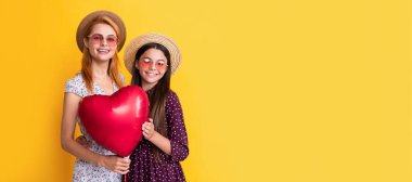 Mother and daughter kid banner, copy space, isolated background. smiling mother and daughter holding love heart balloon on yellow background