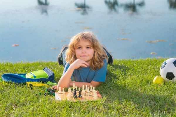 Chess school outdoor. Child laying on grass in spring park and think about chess game. Child education concept. Intelligent, smart and clever school kids. Dream kids and childhood concept