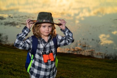 Dürbünlü çocuk dışarıda geziyor. Yaz günü sırt çantalı bir gezgin. Vahşi hayatı keşfeden küçük bir çocuğun portresi. Yürüyüş ve macera konsepti