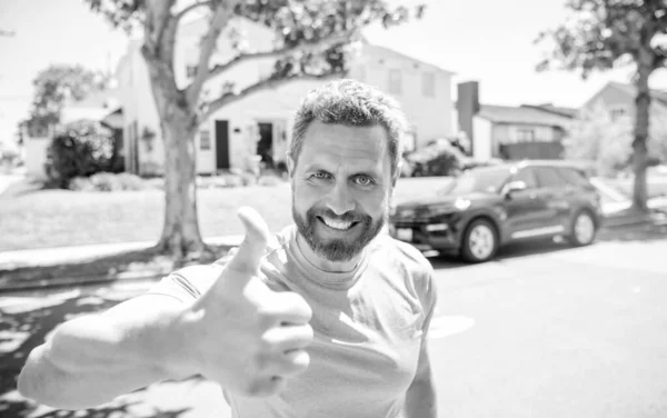 感情成熟的男人在做手势 在新的房子背景上 户外快乐的男人 表达积极的情绪 一个快乐的男人 留着胡子 露出大拇指 男性特写人脸肖像 — 图库照片