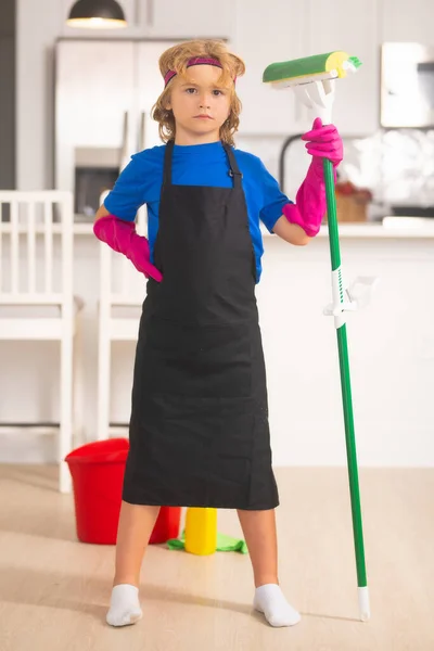 Child cleans at home concept. Kid cleaning with mop to help with housework. Little cute boy sweeping and cleaning, on kitchen background