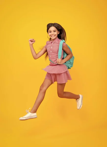 Schoolgirl in school uniform with school bag. Schoolchild, teen student hold backpack on yellow isolated background. Crazy run and jump