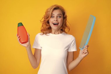 Redhead woman with a comb, isolated on yellow background. Woman hold bottle shampoo and conditioner