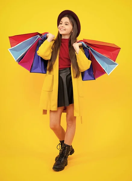 Winter shopping sale. Beautiful fashion teenager child girl with shopping bags on yellow background. Shopaholic shopping and fashion. Kid with shopping sale bags. Smiling girl