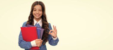 winking child long curly hair hold school workbook isolated on white show ok gesture, high school. Banner of schoolgirl student. School child pupil portrait with copy space