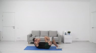Sporcu adam spor kaslarını spor minderinde çıtırdatıyor. Sporcu karın kasları için spor çatırdatma egzersizi yapar. Sporcu karın kaslarını çalıştırıyor. Spor konsepti. Spor spikeri evde karın kaslarını çalıştırıyor..