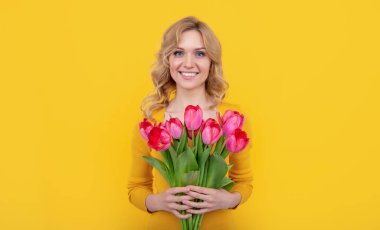 Sarı arka planda bahar lale çiçekleriyle gülümseyen genç kız..