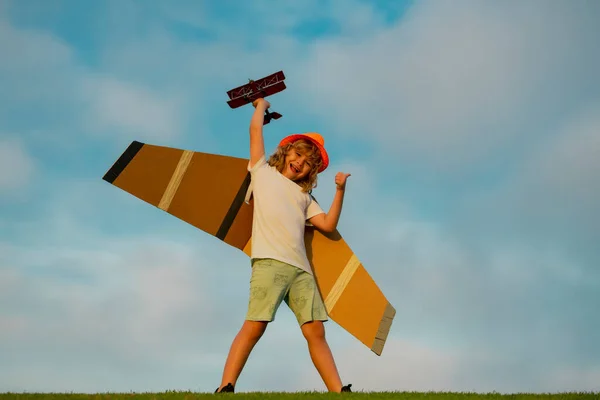 Child pilot aviator with with paper wings or toy airplane dreams of traveling in summer in nature