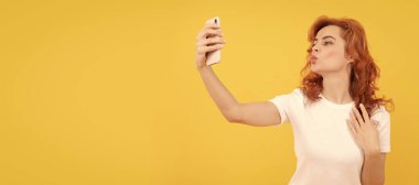 Kadın hava öpücüğü veriyor, fotoğraf makinesi ile selfie çekiyor, sarı arka plan, oto portre fotoğrafı. İzole edilmiş yüz portresi, taklit alanı olan pankart