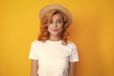 Hasır şapkalı genç kızıl saçlı kadın, şaşırmış yüz ifadesi, sarı arka planda soyutlanmış. Yaz yaşam tarzı stüdyo resmi
