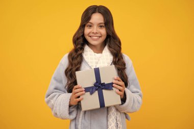 Sarı arka planda izole edilmiş hediye kutusunu tutan genç kız çocuğu. Çocukların doğum günü hediyesi.