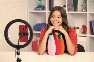 Teen girl hold hair conditioner or shampoo bottle in front of camera for vlog. Teenager working as blogger, recording video blog. Happy girl face, positive and smiling emotions