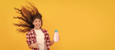 kid use shower gel. happy teen girl with shampoo bottle. shampooing hair in salon. Banner of child girl hair care, studio poster header with copy space