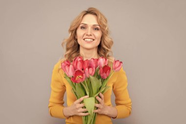 Gri arka planda bahar tatili için çiçekleri tutan mutlu bir kadın..