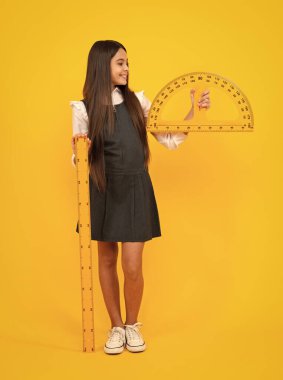 Back to school. School girl hold ruler measuring isolated on yellow background. Happy girl face, positive and smiling emotions
