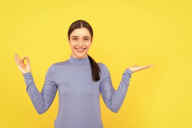 Reklam. Neşeli kadın fotokopi alanında ürün sunuyor. Güzellik ve moda. Kadın manken. Genç kız gösterisi tamam. Sarı arka planda bayan portresi. pozitif duyguları ifade et.