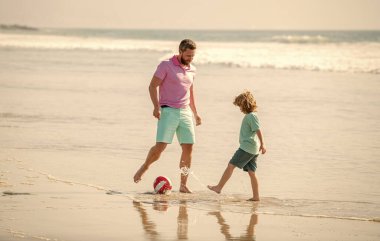 Hafta sonu aile günü. Baba ve çocuk dışarıda eğleniyor. Çocukluk ve ebeveynlik. Aile tatilleri. Spor aktivitesi. Baba ve oğul plajda futbol oynuyorlar. Baba ve çocuk yaz günü.