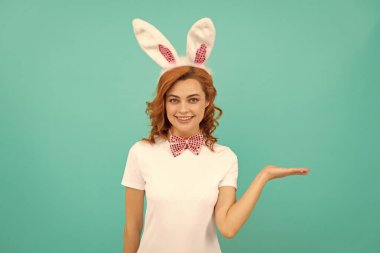 Tavşan kulaklı ve papyonlu mutlu Paskalya kadını mavi arka planda fotokopi alanı olan ürünü sunuyor..