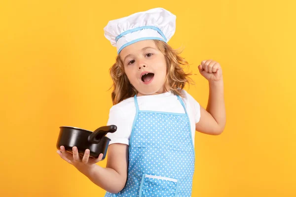 Funny kid chef cook with kitchen pot stockpot. Cooking, culinary and kids. Little boy in chefs hat and apron on studio isolated background