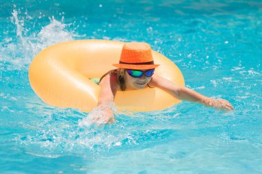 Child in swimming pool on inflatable ring. Little boy swim with orange float. Water toy for kids. Healthy outdoor sport activity for children. Kids beach fun